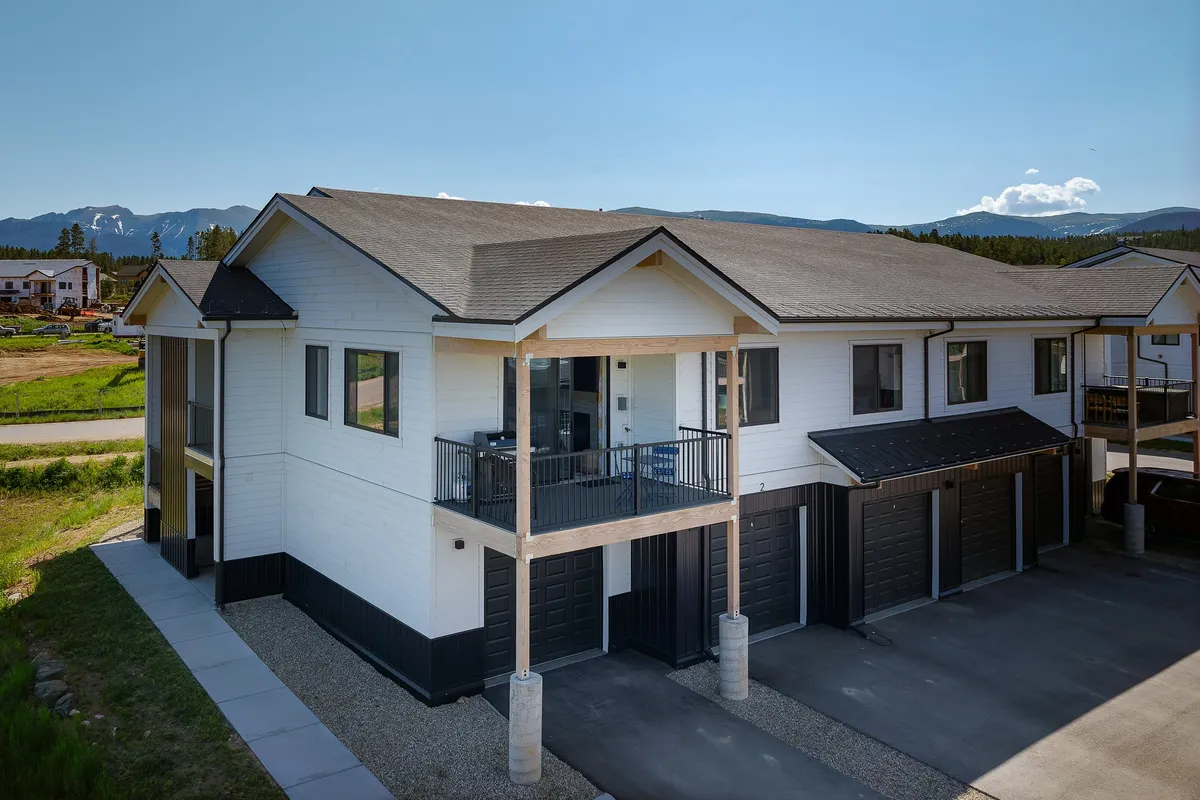 A welcoming exterior shot of the condo building with a spacious balcony overlooking a sweeping mountain vista. The image also shows garage doors—ideal for storing outdoor gear—and hints at relaxing moments after a day of adventure.