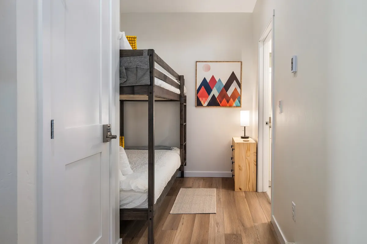 The image features a bunk bed with vibrant artwork on the wall and a nightstand with a lamp. The room exudes a playful, relaxed mood that’s perfect for children, complete with spaces for bedtime stories and bonding moments.