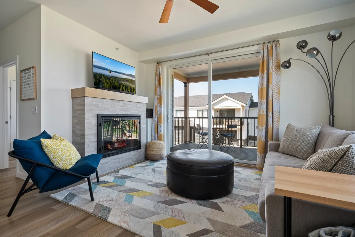 A bright interior living area with a fireplace, sofa, coffee table, TV, and large balcony doors that open up to the deck. The space feels open and seamlessly connects the indoor living area with the outdoor deck.