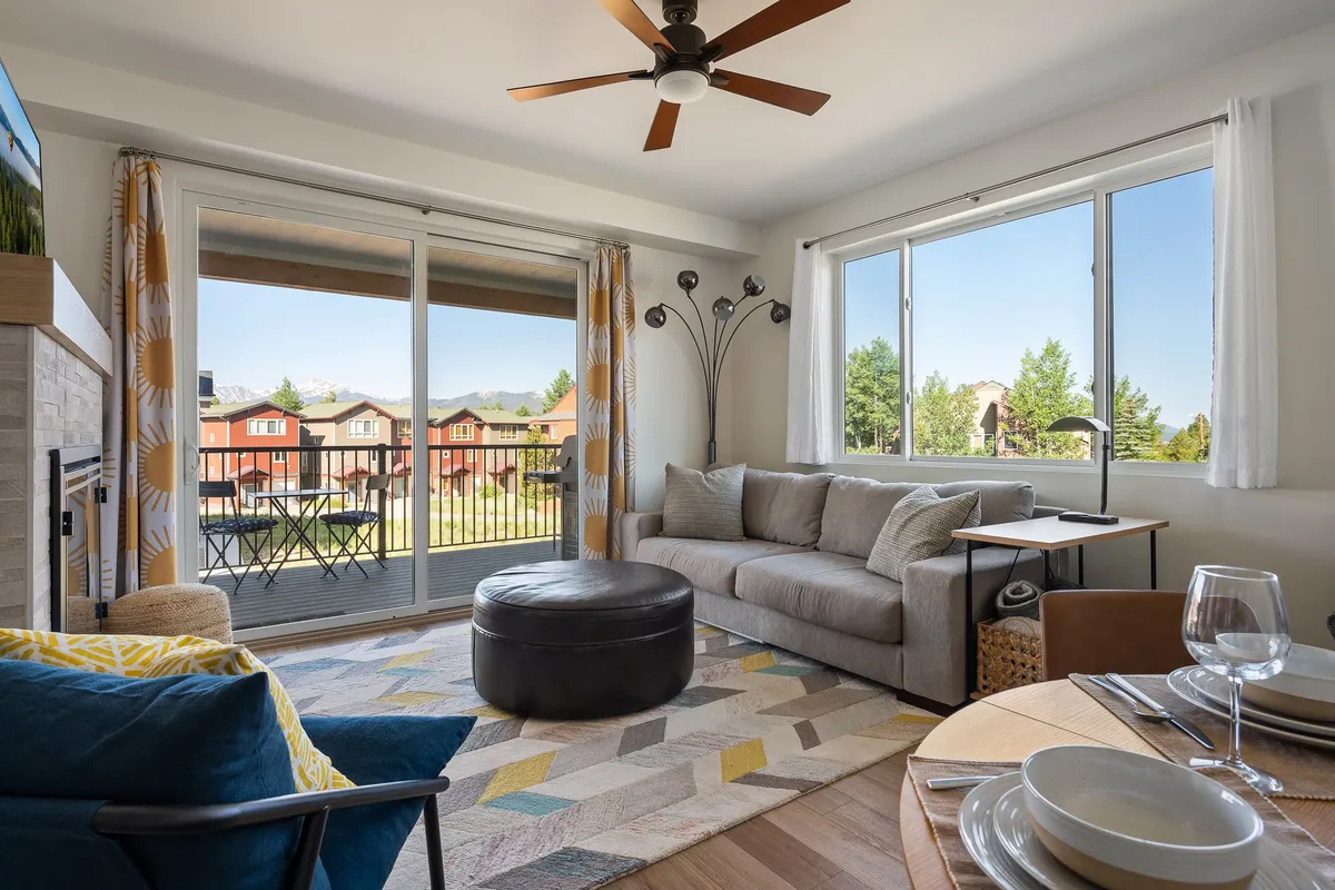 A cozy living area featuring a comfortable sofa and coffee table, with a view extending through a sliding door to an outdoor space. The decor includes a stylish lamp and an area rug, all bathed in natural light.