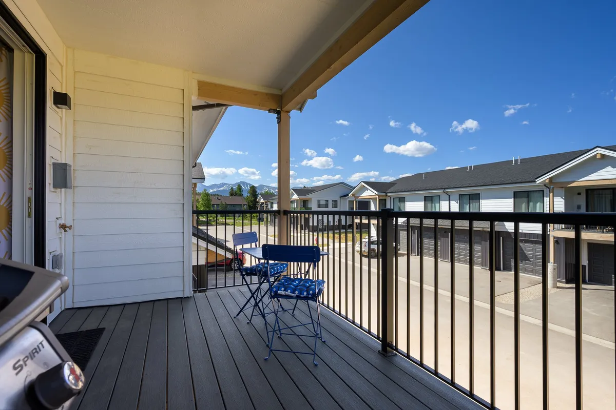 A cozy balcony setup featuring blue chairs, a grill, and balcony railing, all oriented to maximize enjoyment of natural light and sunset views. The space feels casual and welcoming, ideal for socializing or relaxing outdoors.