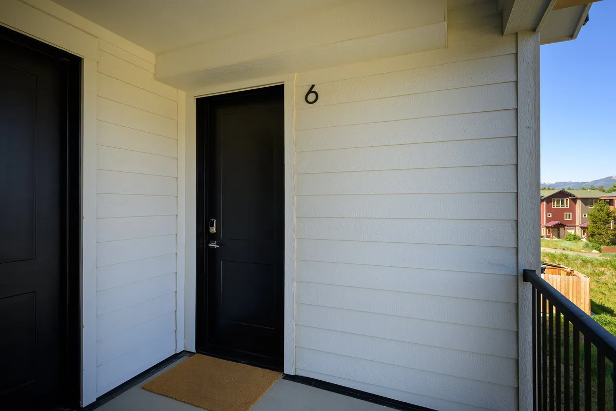 An inviting exterior view featuring a black front door with house number 6 and a doormat. The entryway is welcoming, suggesting a home that is ready to greet guests and pets alike. The scene communicates a sense of arrival in a comfortable, pet-welcoming environment.