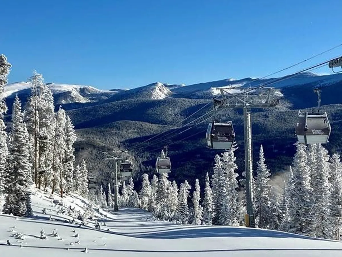 This image features a gondola lift rising above snow-covered trees with a dramatic mountain range in the background. The scene captures the thrill of alpine adventure and the allure of Winter Park Resort's outdoor activities, highlighting both winter sports and mountain exploration.
